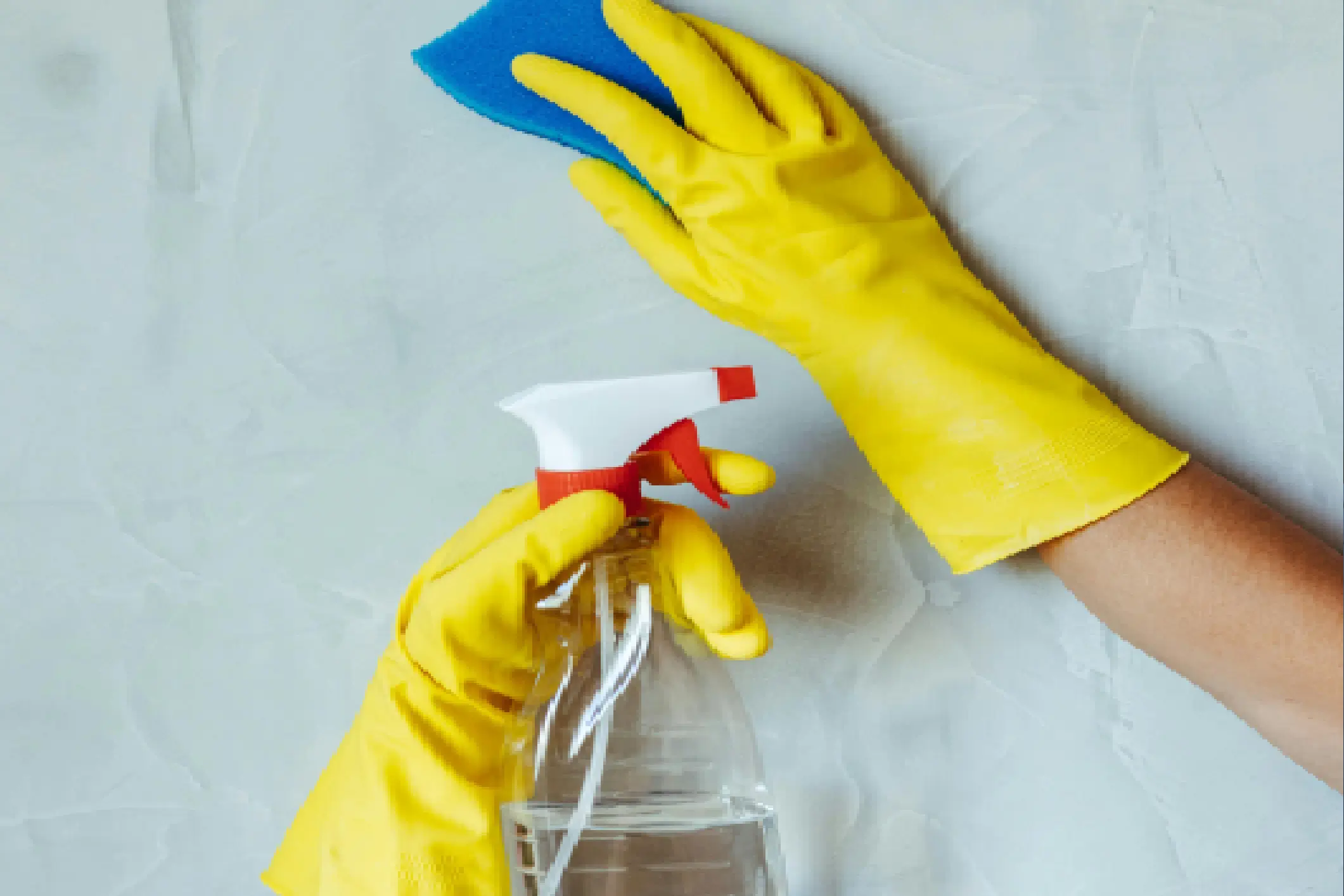 Hands in yellow gloves holding a spray bottle for cleaning.