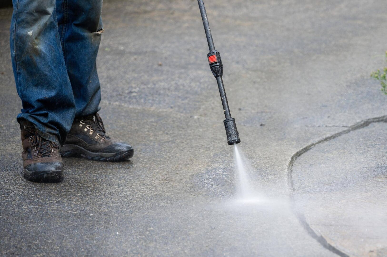Person using a pressure washer to clean a concrete surface.